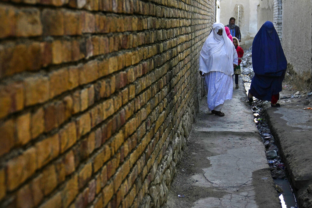 Afghans pass in an alley along an open sewer in a poor neighborhood of Kabul, Afghanistan, Sunday, Feb. 20, 2022. (AP Photo/Hussein Malla)