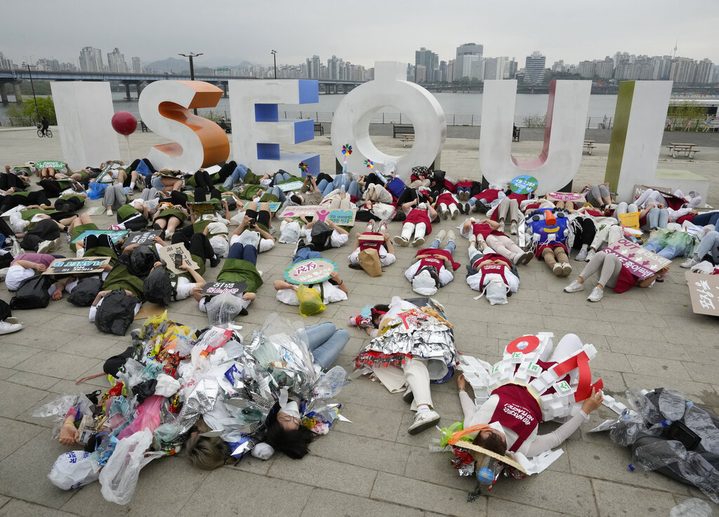 Environmental activists, some wearing outfits made from plastic waste, lie down on the ground during a campaign to mark Earth Day against climate change in Seoul, South Korea, Friday, April 22, 2022. (AP Photo/Ahn Young-joon)
