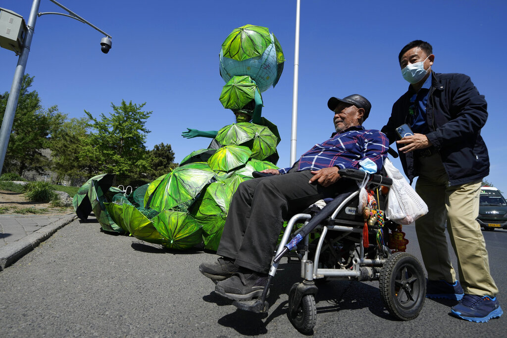 A man wearing a mask helps a man in a wheel chair past by Chinese artist Kong Ning with her latest work 