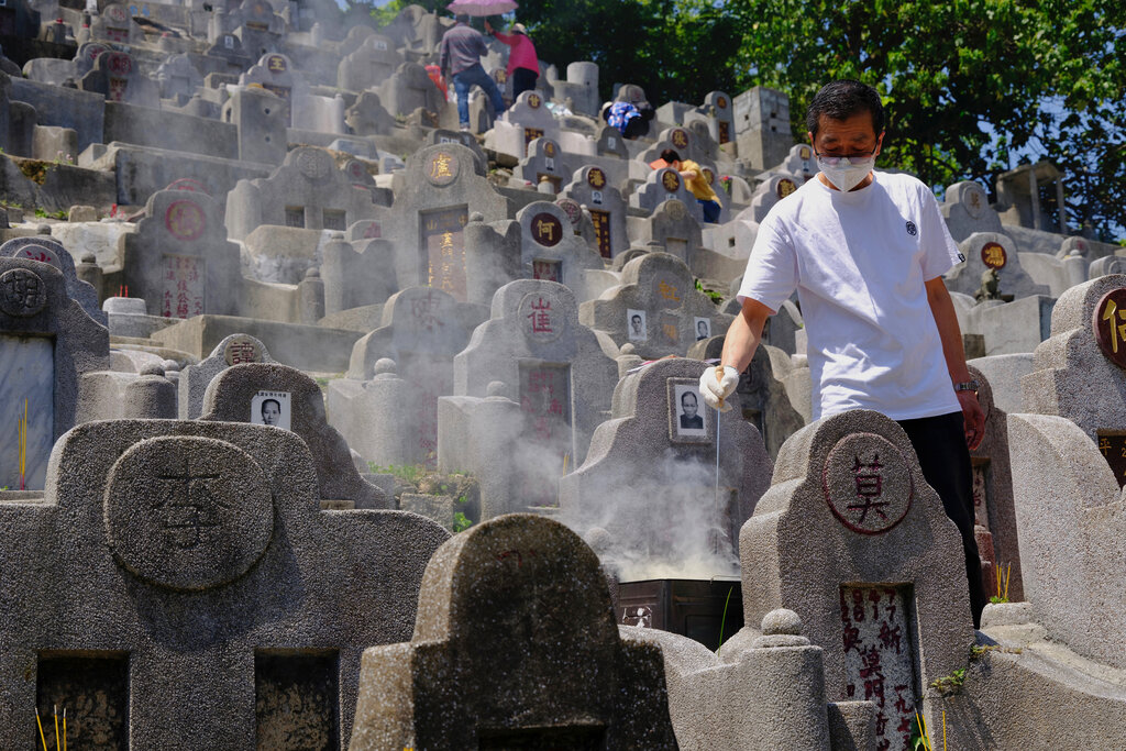 A man wearing face mask burns paper money at the gravesite of a relative in a cemetery during the Chinese Ching Ming, or Tomb Sweeping Day, in Hong Kong Tuesday, April 5, 2022. Thousands of Hong Kong residents pay respects to their ancestors and relatives during the annual festival. (AP Photo/Vincent Yu)