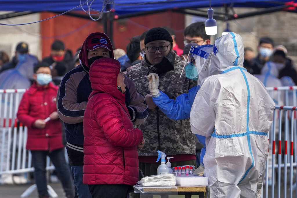 A health worker in protective suit takes a throat swab sample from a resident at an outdoor coronavirus testing site, Wednesday, March 23, 2022, in Beijing, China. A fast-spreading variant known as 