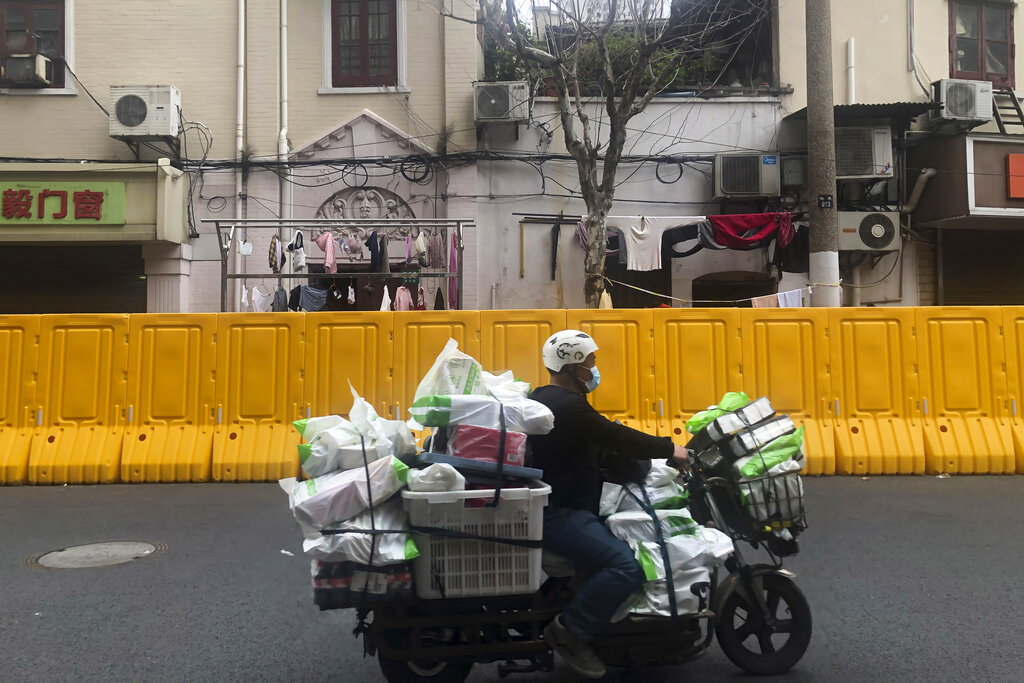 A delivery man passes by barriers set up to lock down a community in Shanghai, China, Wednesday, March 30, 2022. As millions of Shanghai residents line up for coronavirus tests in the closed-down metropolis, authorities are promising tax cuts for shopkeepers and to keep its busy port functioning to limit disruptions to industry and trade. (AP Photo/Chen Si)