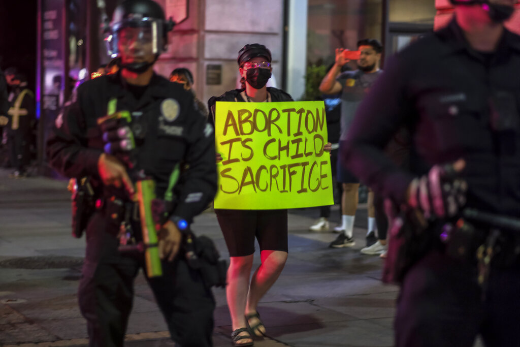 A demonstrator holding a sign walks by police officers after a confrontation between demonstrators and police near Pershing Square following a protest outside the U.S. Courthouse in response to leaked draft of the Supreme Court's opinion to overturn Roe v. Wade in Los Angeles, Tuesday, May 3, 2022. (AP Photo/Ringo H.W. Chiu)