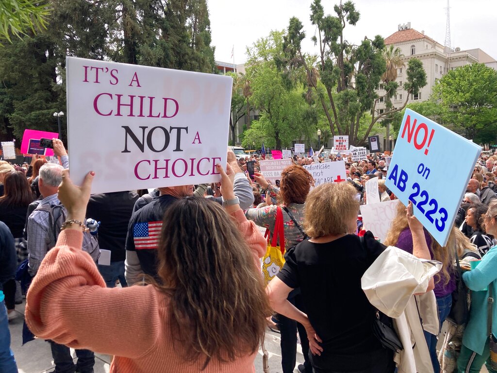 A woman holds a sign opposing a bill in the state Legislature on Tuesday, April 19, 2022, in Sacramento, Calif. Hundreds of people rallied against a bill in the state Assembly that seeks to strengthen state laws preventing prosecution of women for the death of an unborn fetus. (AP Photo/Adam Beam)
