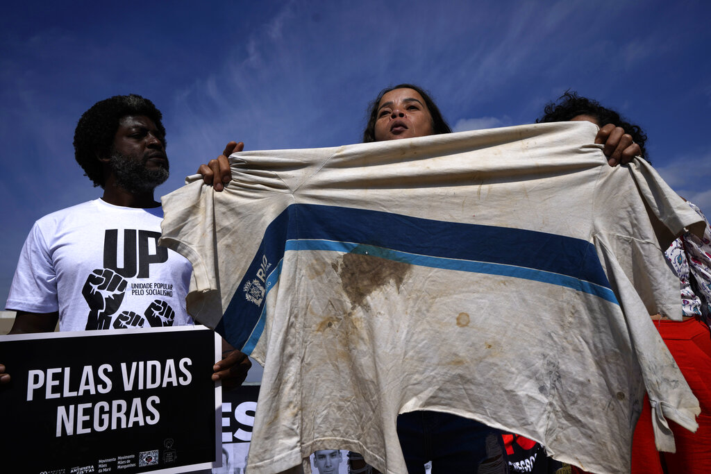 Bruna Silva holds up the blood-stained school shirt she says was used by her 13-year-old son when he was killed during a police operation in the favela da Mare in Rio de Janeiro, during a protest demanding justice outside the Supreme Court in Brasilia, Brazil, Thursday, May 12, 2022, the eve of the anniversary of the abolition of slavery. Brazil abolished slavery on May 13, 1888 in Brazil. The sign reads 