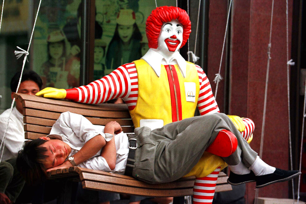 FILE - In this May 27, 1998, file photo, Chinese man sleeps with his legs draped across a Ronald McDonald mannequin outside the McDonald's restaurant at the south end of Beijing's Tiananmen Square. McDonald’s opened its first Chinese outlet in 1990. (AP Photo/Greg Baker, File)