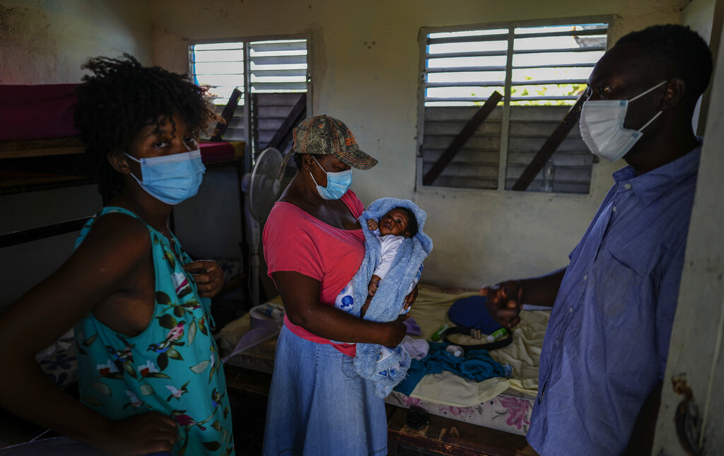 Loverie Horat, left, stands by her mother holding her 24-day-old daughter Maylie Dhavavaise as her husband Maximaud Cherizad looks on, at a campground being used to house the large group of Haitian migrants with whom they are traveling, in Sierra Morena in Cuba's Villa Clara province, Thursday, May 26, 2022. A vessel carrying more than 800 Haitians trying to reach the United States wound up instead on the coast of central Cuba, in what appeared to be the largest group seen yet in a swelling exodus from crisis-stricken Haiti. (AP Photo Ramon Espinosa)
