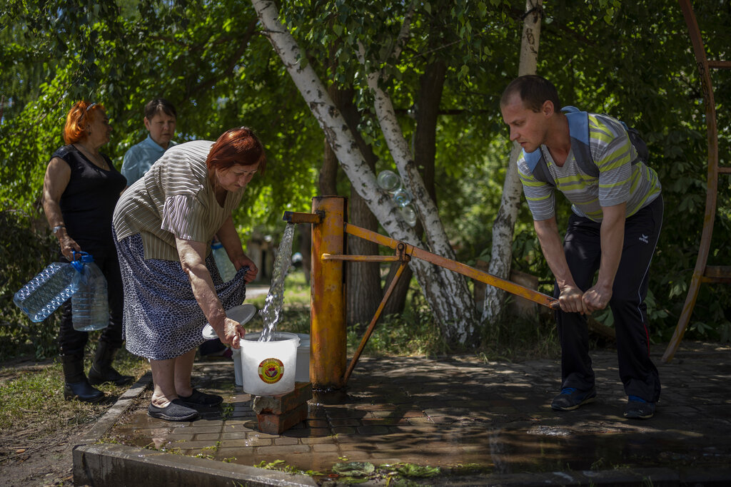 Residents gather to collect water from a pump in the street in Sloviansk, Ukraine, on Thursday, June 2, 2022. In towns and cities near the fighting in eastern Ukraine, artillery and missile strikes have downed power lines and punched through water pipes, leaving many without electricity or water as repair crews race to repair the damage. (AP Photo/Elena Becatoros)