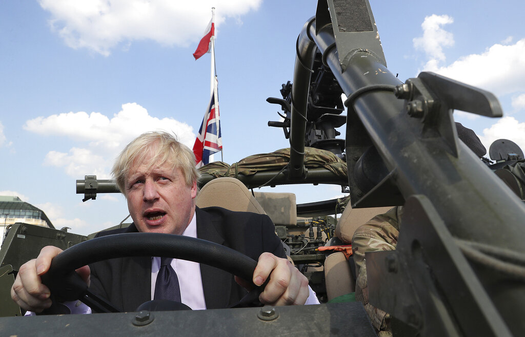 FILE - In this Thursday, June 21, 2018 file photo Britain's then Foreign Secretary Boris Johnson talks to a British armed forces serviceman based in Orzysz, in northeastern Poland, during a ceremony at the Tomb of the Unknown Soldier and following talks on security with his Polish counterpart Jacek Czaputowicz in Warsaw, Poland. A British judge has ruled that former Foreign Secretary Boris Johnson will be summoned to court to answer questions about his possible misconduct in public office during the Brexit referendum campaign in 2016. (AP Photo/Czarek Sokolowski, File)