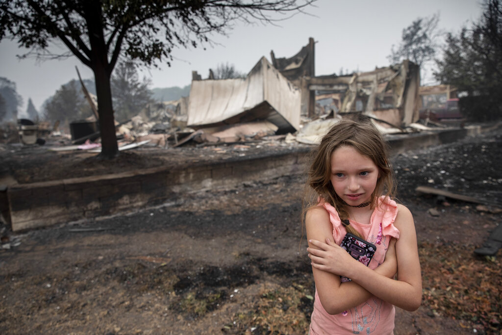 FILE - Ellie Owens, 8, from Grants Pass, Ore., looks at damage from wildfires that devastated the region in Talent, Ore., on Sept. 11, 2020. Climate change and an enduring drought have fanned the frequency and intensity of wildfires in the West in recent years.(AP Photo/Paula Bronstein, File)