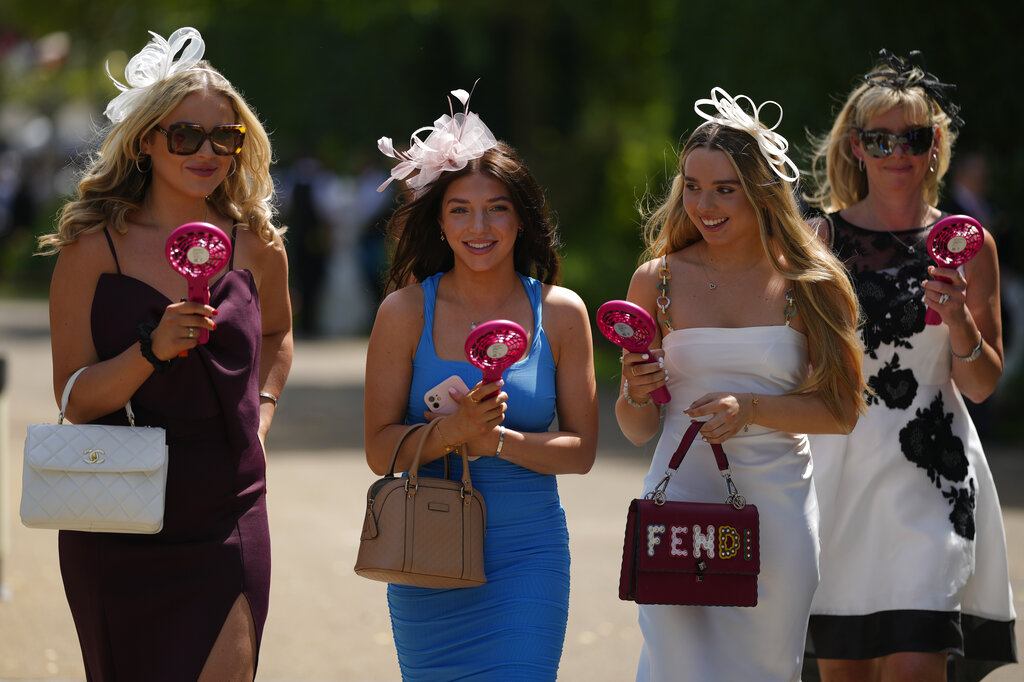 Racegoers carrying portable fans to keep cool arrive for the fourth day of the Royal Ascot horserace meeting, at Ascot Racecourse, in Ascot, England, Friday, June 17, 2022. (AP Photo/Alastair Grant)