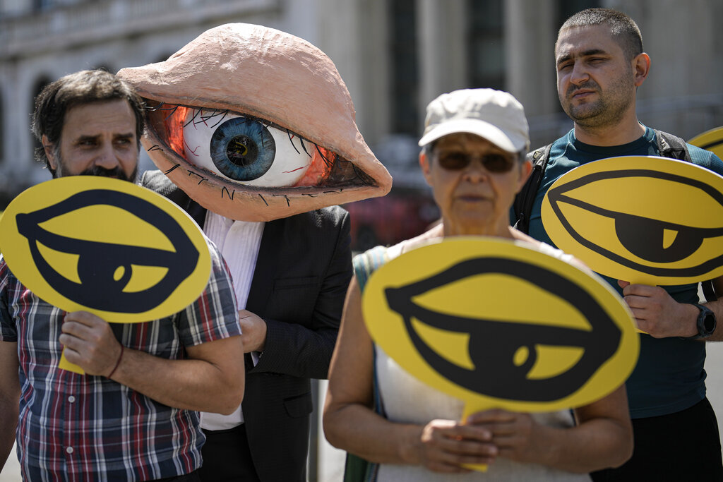 An activist wears a mask depicting a large eyeball during a protest against planned updates of the country's national security laws, after a draft was leaked to the media earlier this month, in Bucharest, Romania, Wednesday, June 22, 2022. Dozens of activists gathered outside the government headquarters to protest against proposed changes to the laws that offer increased power to Romania's intelligence service (SRI), which include an obligation for citizens and companies to offer support to the service if requested. (AP Photo/Vadim Ghirda)