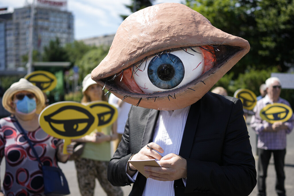 An activist wears a mask depicting a large eyeball during a protest against planned updates of the country's national security laws, after a draft was leaked to the media earlier this month, in Bucharest, Romania, Wednesday, June 22, 2022. Dozens of activists gathered outside the government headquarters to protest against proposed changes to the laws that offer increased power to Romania's intelligence service (SRI), which include an obligation for citizens and companies to offer support to the service if requested. (AP Photo/Vadim Ghirda)