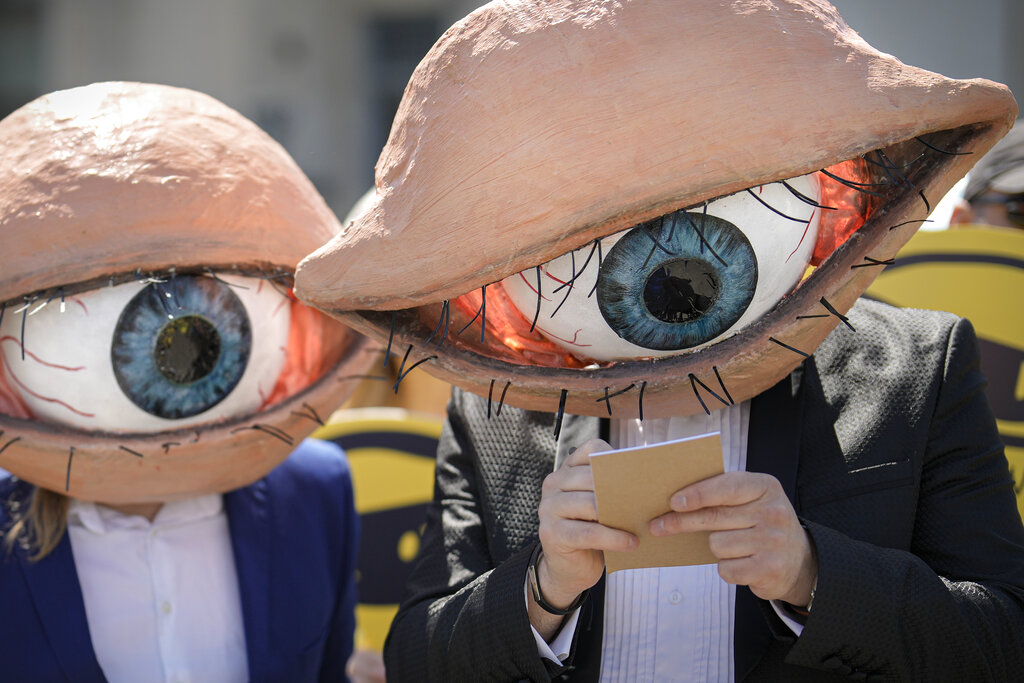 Activists wearing masks depicting large eyeballs attend a protest against planned updates of the country's national security laws, after a draft was leaked to the media earlier this month, in Bucharest, Romania, Wednesday, June 22, 2022. Dozens of activists gathered outside the government headquarters to protest against proposed changes to the laws that offer increased power to Romania's intelligence service (SRI), which include an obligation for citizens and companies to offer support to the service if requested. (AP Photo/Vadim Ghirda)