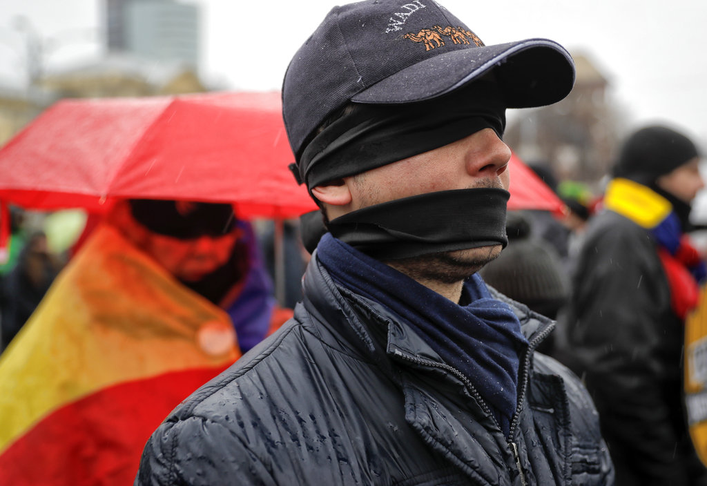 People take part in a flash mob in Bucharest, Romania, Sunday, Dec. 17, 2017. Protesters braved low temperatures and rain covering their mouths and eyes with black ribbons during a flash mob outside the government headquarters against planned modifications to Romanian justice legislation that critics say would render it less effective in punishing high-level corruption. (AP Photo/Vadim Ghirda)