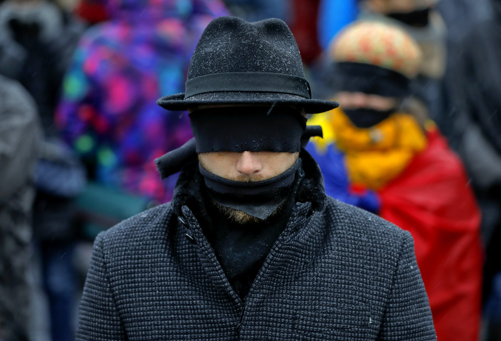 A man takes part in a flash mob in Bucharest, Romania, Sunday, Dec. 17, 2017. Protesters braved low temperatures and rain covering their mouths and eyes with black ribbons during a flash mob outside the government headquarters against planned modifications to Romanian justice legislation that critics say would render it less effective in punishing high-level corruption. (AP Photo/Vadim Ghirda)