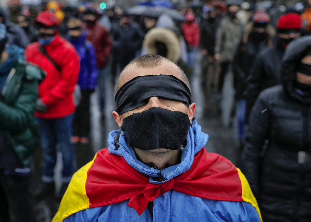 A man stands as he takes part in a flash mob in Bucharest, Romania, Sunday, Dec. 17, 2017. Protesters braved low temperatures and rain covering their moths and eyes with black ribbons during a flash mob outside the government headquarters against planned modifications to Romanian justice legislation that critics say would render it less effective in punishing high-level corruption. (AP Photo/Vadim Ghirda)