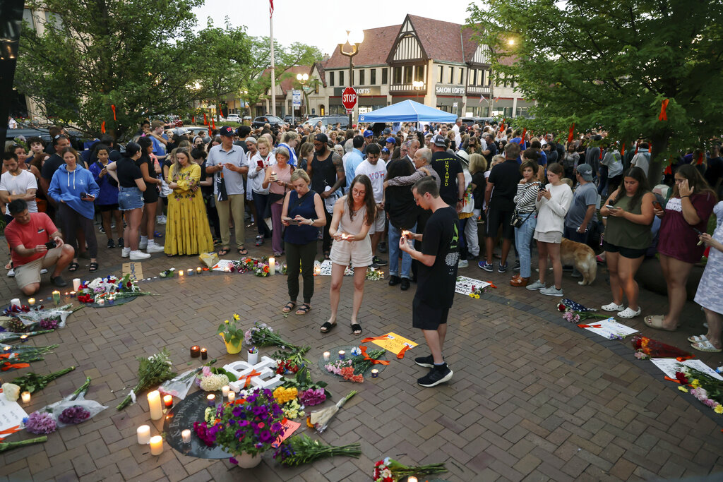 Dozens of mourners gather for a vigil near Central Avenue and St. Johns Avenue in downtown Highland Park, one day after a gunman killed at least seven people and wounded dozens more by firing an AR-15-style rifle from a rooftop onto a crowd attending Highland Park's Fourth of July parade, Tuesday, July 5, 2022 in Highland Park, Ill.. (Anthony Vazquez/Chicago Sun-Times via AP)