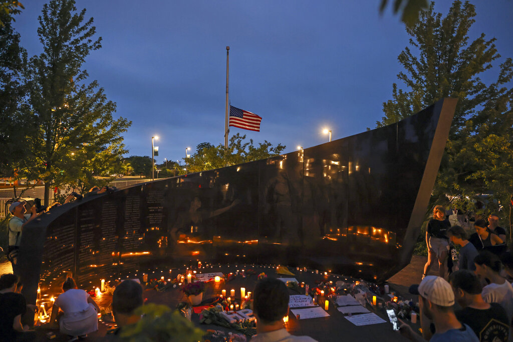 Dozens of mourners gather for a vigil near Central Avenue and St. Johns Avenue in downtown Highland Park, one day after a gunman killed at least seven people and wounded dozens more by firing an AR-15-style rifle from a rooftop onto a crowd attending Highland Park's Fourth of July parade, Tuesday, July 5, 2022 in Highland Park, Ill.. (Anthony Vazquez/Chicago Sun-Times via AP)