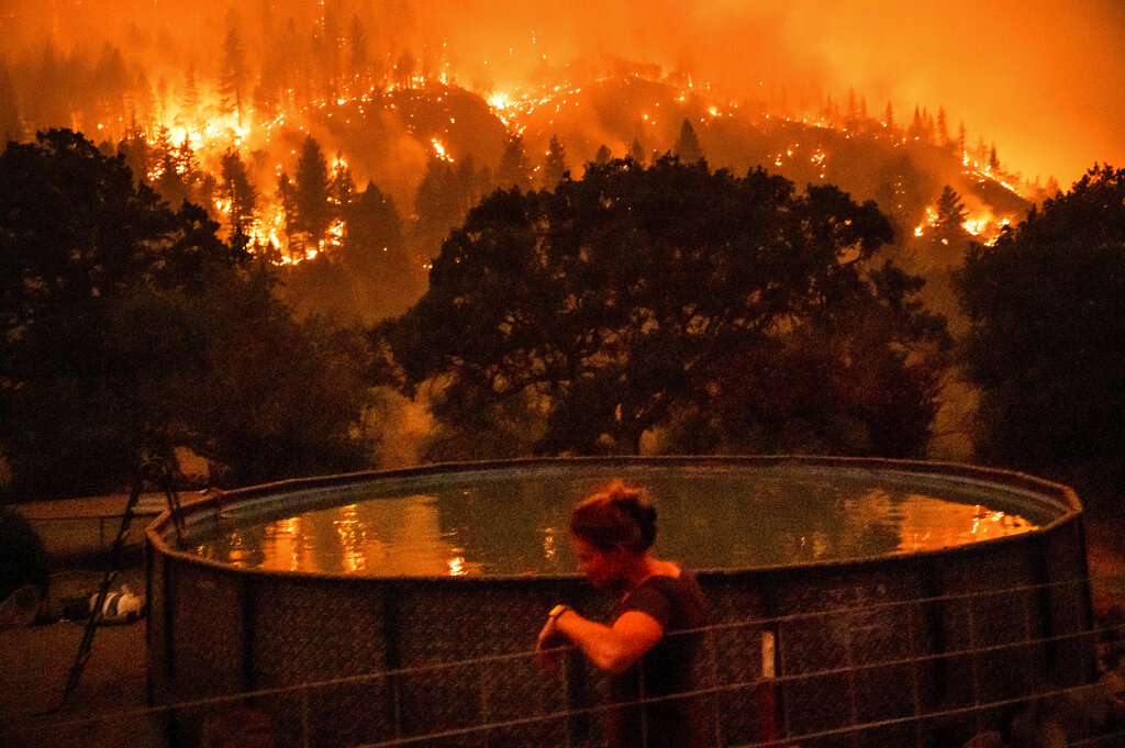Angela Crawford leans against a fence as a wildfire called the McKinney fire burns a hillside above her home in Klamath National Forest, Calif., on Saturday, July 30, 2022. Crawford and her husband stayed, as other residents evacuated, to defend their home from the fire. (AP Photo/Noah Berger)