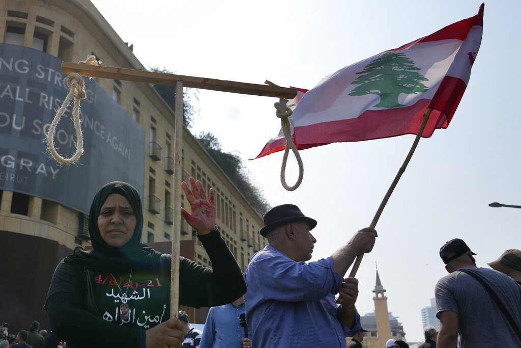The mother of a victim of the deadly 2020 Beirut port explosion shows her palm painted in red as she holds up a mock gallows during  a march to mark the second anniversary of the massive blast, Thursday, Aug. 4, 2022, in Beirut, Lebanon. A large block of Beirut's giant port grain silos, shredded by the massive explosion two years ago, collapsed on Thursday as hundreds marched in the Lebanese capital to mark the anniversary of the blast that killed scores. (AP Photo/Hassan Ammar)