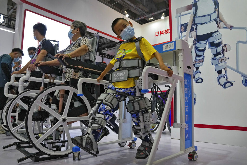 A child and other visitors try out a Chinese-made robotic legs used to support disability people during the World Robot Conference at the Yichuang International Conference and Exhibition Centre in Beijing, Thursday, Aug. 18, 2022. (AP Photo/Andy Wong)