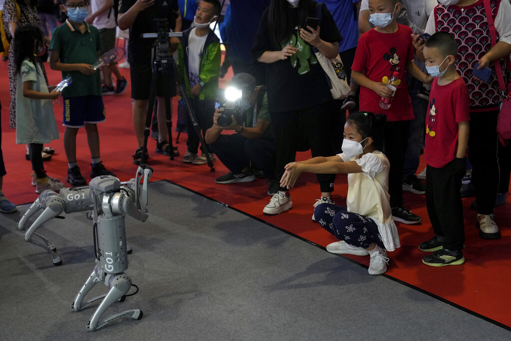 A child wearing a face mask gestures as she plays with a Unitree Go 1 intelligent side-follow robot during the World Robot Conference at the Yichuang International Conference and Exhibition Centre in Beijing, Thursday, Aug. 18, 2022. (AP Photo/Andy Wong)