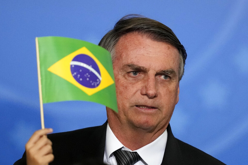 Brazil's President Jair Bolsonaro looks past the hand of a child holding a Brazilian national flag during the ceremony to receive the reliquary containing the heart of Brazil's former emperor Dom Pedro I, at the Planalto Presidential Palace, in Brasilia, Brazil, Tuesday, Aug. 23, 2022. The heart arrived for display during the celebrations of Brazil's independence bicentennial on Sept. 7. (AP Photo/Eraldo Peres)