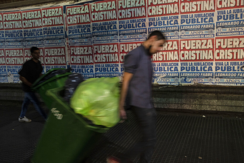 Restaurant workers carry trash next to posters that read, in Spanish, 