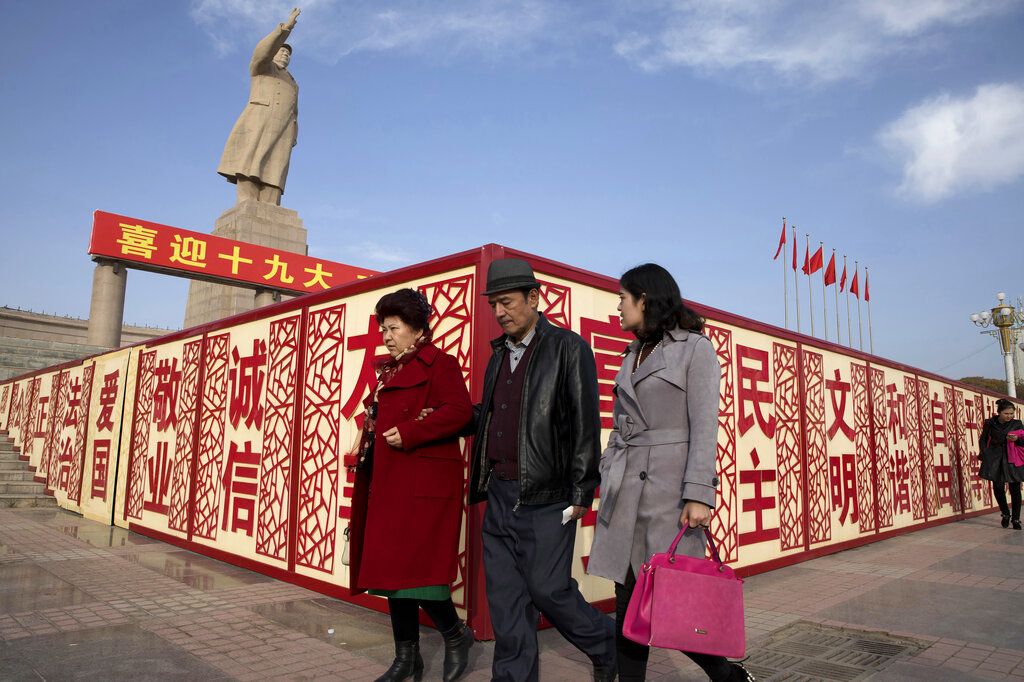FILE - Residents walk past a statue of the late Chinese leader Mao Zedong near billboards reading 