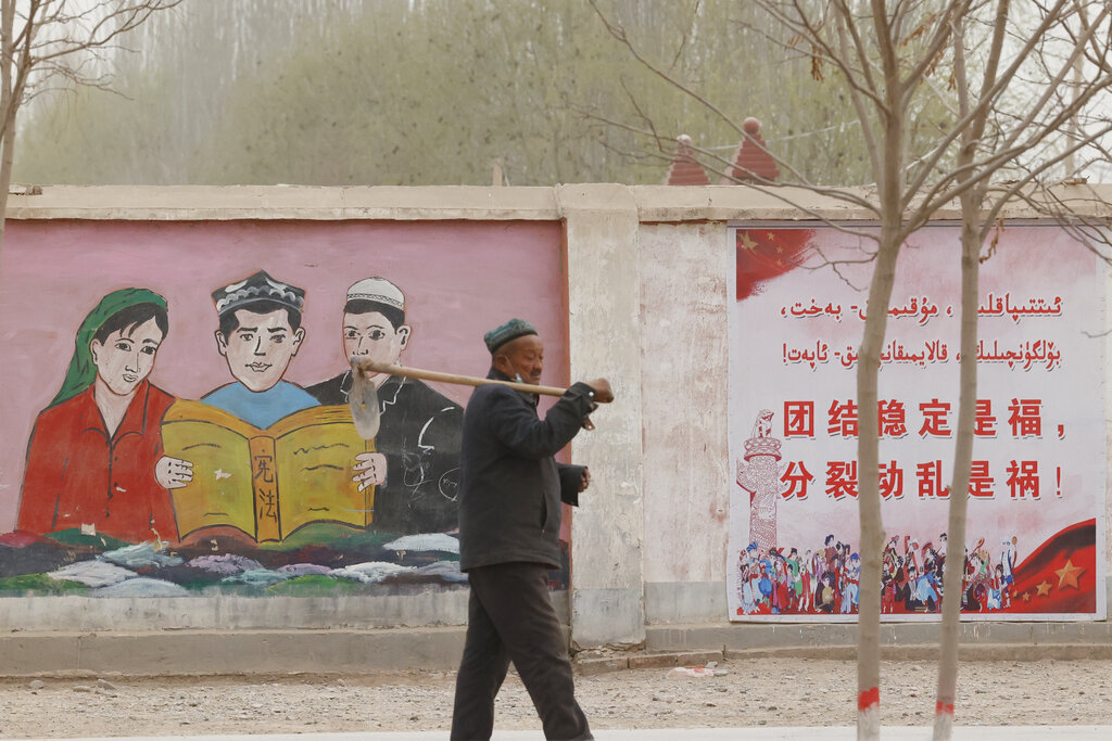 FILE - A farmer walks past government propaganda depicting ethnic minority residents reading the constitution with slogans which reads, 