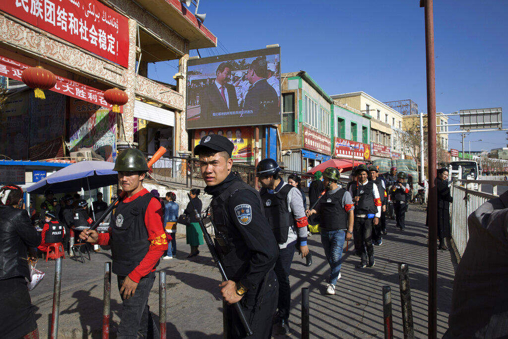 FILE - Armed civilians patrol the area outside the Hotan Bazaar where a screen shows Chinese President Xi Jinping in Hotan in western China's Xinjiang region, Nov. 3, 2017. China's discriminatory detention of Uyghurs and other mostly Muslim ethnic groups in the western region of Xinjiang may constitute crimes against humanity, the U.N. human rights office said in a long-awaited report Wednesday, Aug. 31, 2022, which cited 