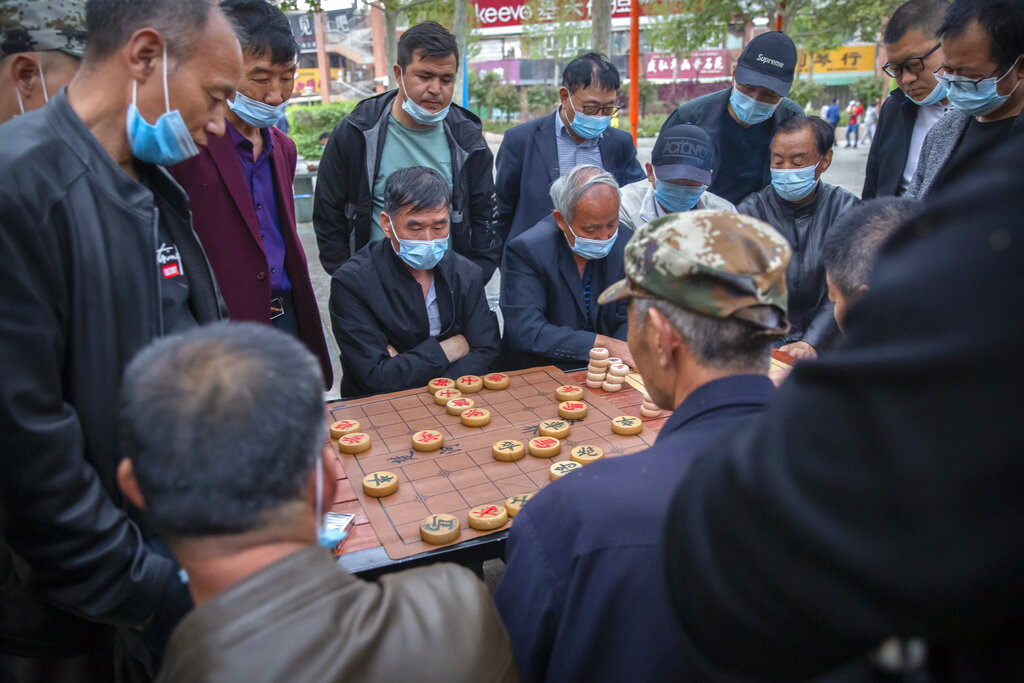 Men play Chinese chess as others watch at a public square in Aksu in western China's Xinjiang Uyghur Autonomous Region, as seen during a government organized trip for foreign journalists, Tuesday, April 20, 2021. In a report issued on Monday, a human rights group appealed to the United Nations to investigate allegations China's government is committing crimes against humanity in the Xinjiang region. (AP Photo/Mark Schiefelbein)
