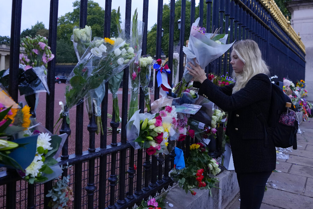 A woman lays flowers at the gate of Buckingham Palace in London, Friday, Sept. 9, 2022. Queen Elizabeth II, Britain's longest-reigning monarch and a rock of stability across much of a turbulent century, died Thursday Sept. 8, 2022, after 70 years on the throne. She was 96. (AP Photo/Kirsty Wigglesworth)