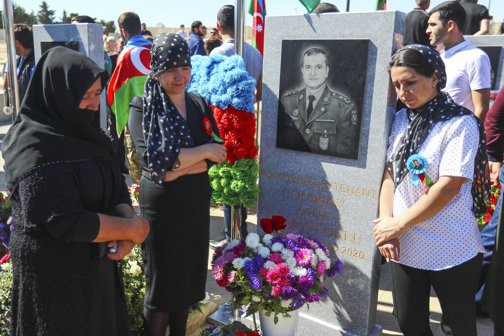 Relatives mourn near a grave of killed Azerbaijan's army soldier at a military cemetery with the graves of the fallen soldiers during the during the fighting over Nagorno-Karabakh in 2020 year, outside Baku, Azerbaijan, Monday, Sept. 27, 2021. Azerbaijan and Armenia are marking the first anniversary of the start of their six-week war in which more than 6,600 people died and that ended with Azerbaijan regaining control of large swaths of territory. Soldiers carrying photos of comrades killed in the war marched Monday through the center of the Azerbaijaini capital Baku. (AP Photo/Aziz Karimov)