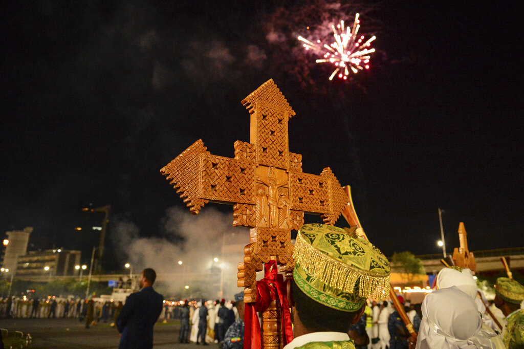 An Ethiopian Orthodox Christian holds a crucifix as fireworks explode to celebrate the eve of the holiday of Meskel in Addis Ababa, Ethiopia Monday, Sept. 26, 2022. The festival commemorates the unearthing of the 
