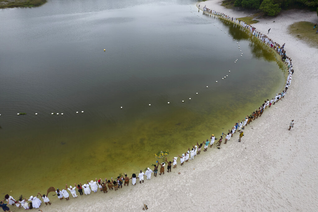 Practitioners of Afro Brazilian faiths gather around the Abaete Lagoon during a protest calling on authorities to take action against a series of environmental offenses in the Abaete dune system, an area they consider sacred, in Salvador, Brazil, Sunday, Sept. 18, 2022. Dressed in white, they marched to the lagoon, the traditional site for most of their rituals, and lined up along the water in a symbolic hug for the area.†(AP Photo/Rodrigo Abd)