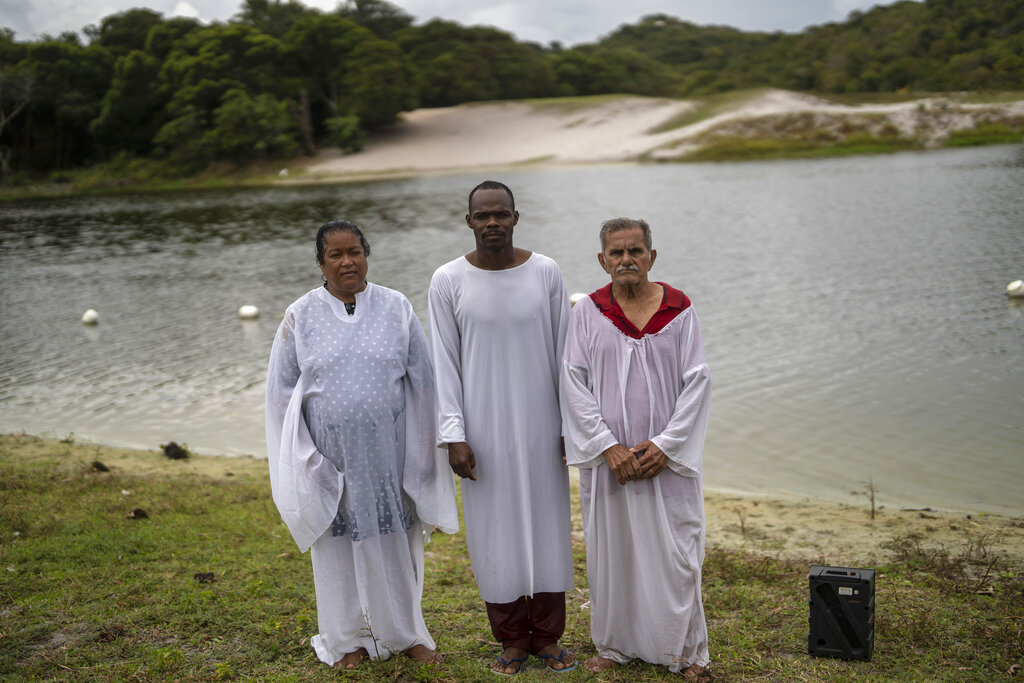 Newly baptized Casa de Oraçao church members Zerilda Souza, 57, from left, Bruno Jesus Santos, 32, and Joao Ferreira, 80, pose for a portrait on the shore of the Abaete Lagoon, in Salvador, Brazil, Sunday, Sept. 18, 2022. While Catholicism is still the largest religion in Brazil, in recent years it has slipped below 50% of the population to lose its status as a majority faith even as evangelical churches have gained. (AP Photo/Rodrigo Abd)
