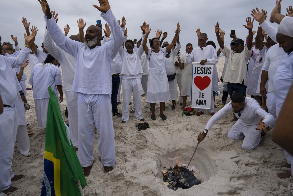 Bishop Wedson Tavares, left, leads his flock in prayer asking God to influence the upcoming election as a congregant burns scrawled prayers on scraps of paper in an area of the Abaete dune system, at a steep rise of sand evangelicals call the 