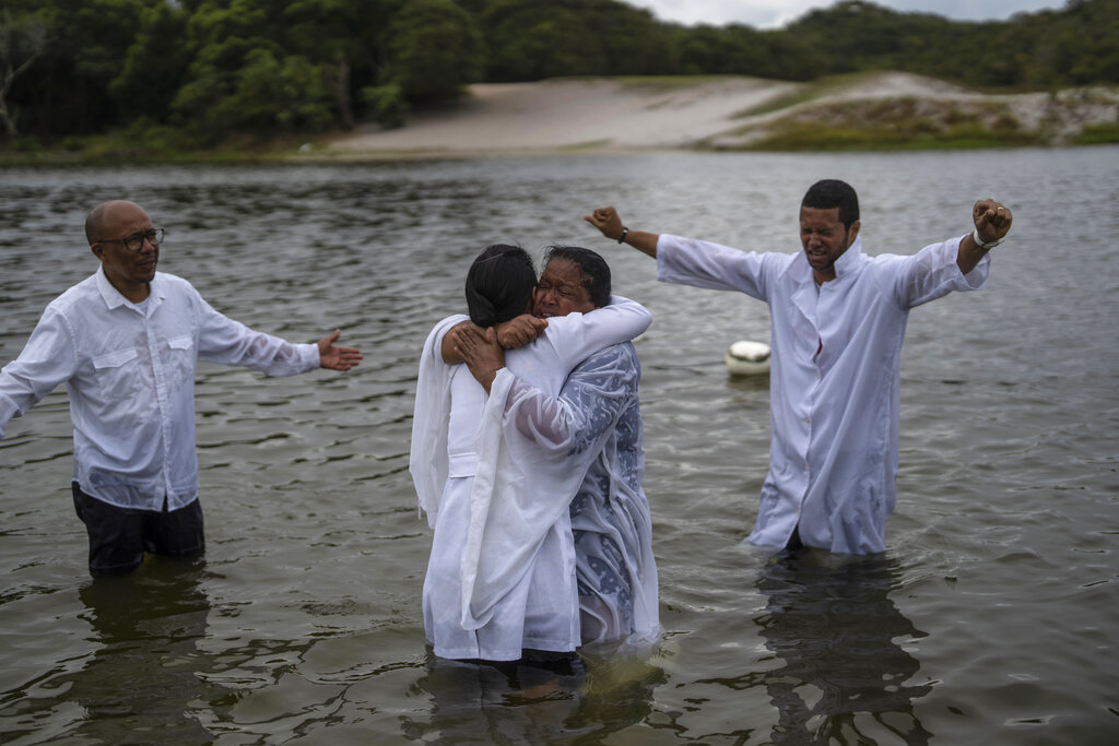 Evangelical Pastor Edy Santos, right, spreads his arms as newly baptized Zerilda Souza, center right, is embraced by a church member, in the Abaete Lagoon, in Salvador, Brazil, Sunday, Sept. 18, 2022. Santos refuses to talk politics with his flock, even when they ask. 
