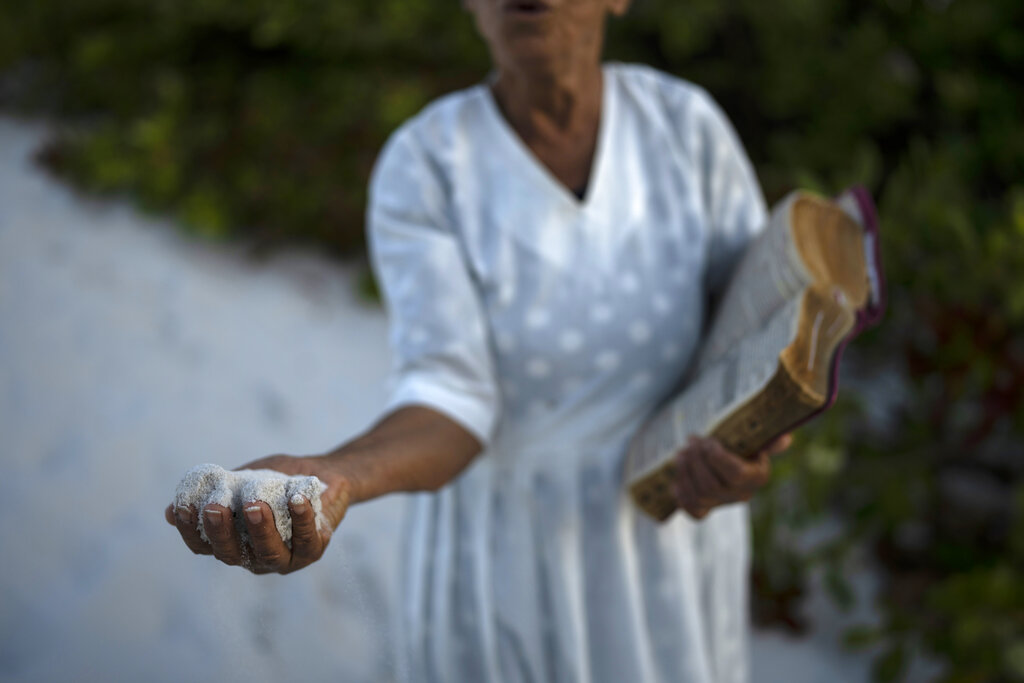 A woman holds a handful of sand as she prays in area of the Abaete dune system, that evangelicals have come to call the 