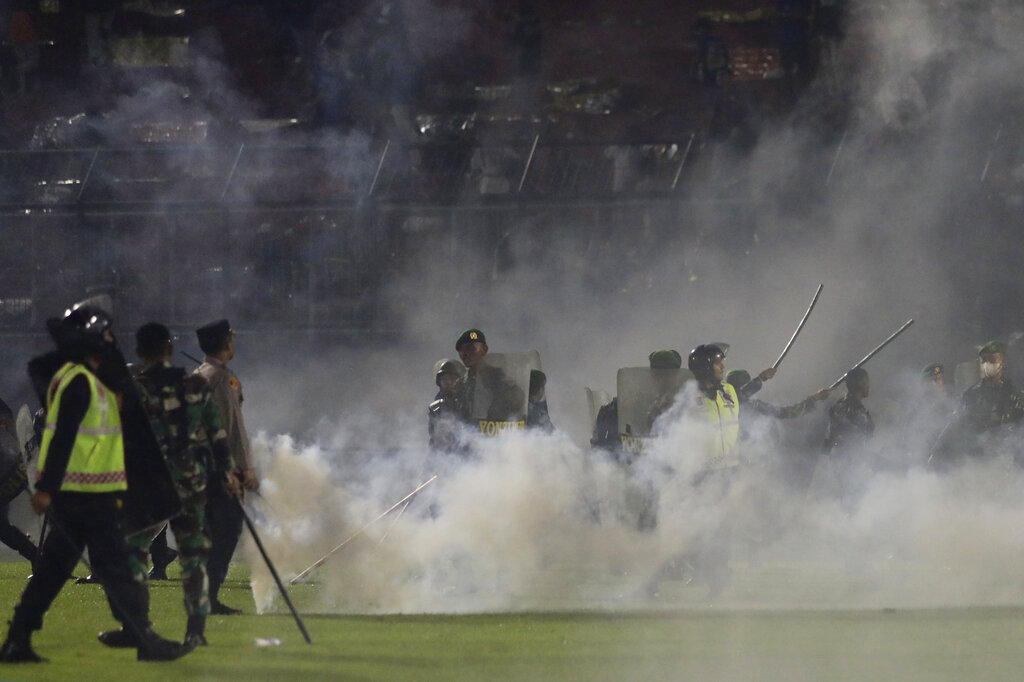 Police officers and soldiers stand amid tear gas smoke after clashes between fans during a soccer match at Kanjuruhan Stadium in Malang, East Java, Indonesia, Saturday, Oct. 1, 2022. Panic following police actions left over 100 dead, mostly trampled to death, police said Sunday. (AP Photo/Yudha Prabowo)
