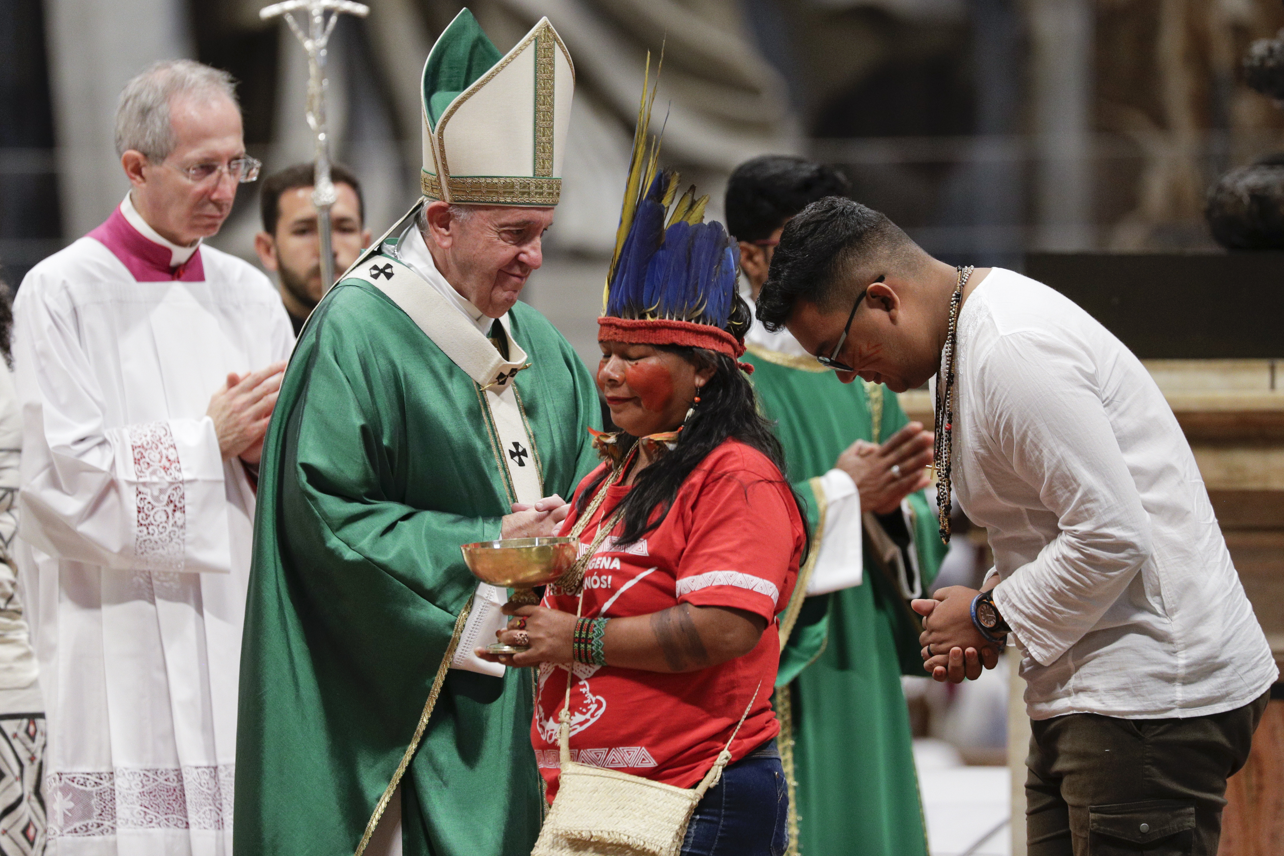 Indigenous peoples, some with their faces painted and wearing feathered headdresses, stand by  Pope Francis as he celebrates an opening Mass for the Amazon synod, in St. Peter's Basilica, at the Vatican, Sunday, Oct. 6, 2019. Pope Francis is opening a divisive meeting on preserving the Amazon and ministering to its indigenous peoples, as he fends off attacks from conservatives who are opposed to his ecological agenda. (AP Photo/Andrew Medichini)
