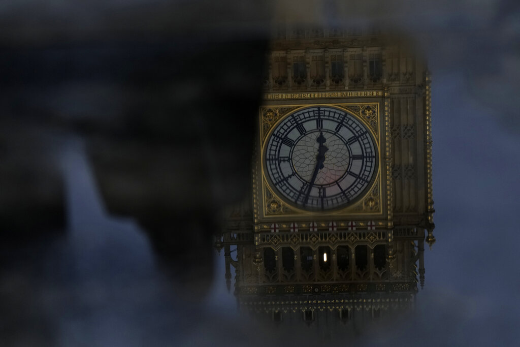 Commuters are reflected in a puddle with the Queen Elizabeth Tower in the background which contains the bell known as 'Big Ben, part of the Palace of Westminster, following a rain shower in London, Thursday, Oct. 20, 2022. British Prime Minister Liz Truss resigned Thursday, bowing to the inevitable after a tumultuous, short-lived term in which her policies triggered turmoil in financial markets and a rebellion in her party that obliterated her authority. (AP Photo/Alastair Grant)