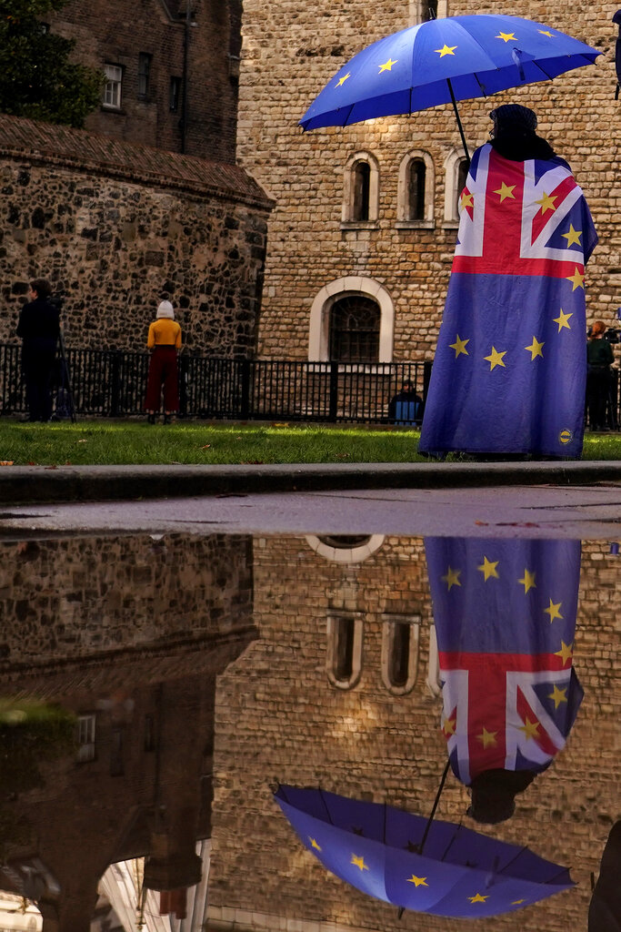 A protestor is reflected in a puddle opposite parliament after Britain's Prime Minister Liz Truss resigned in London, Thursday, Oct. 20, 2022. Truss resigned Thursday, bowing to the inevitable after a tumultuous, short-lived term in which her policies triggered turmoil in financial markets and a rebellion in her party that obliterated her authority.(AP Photo/Alberto Pezzali)