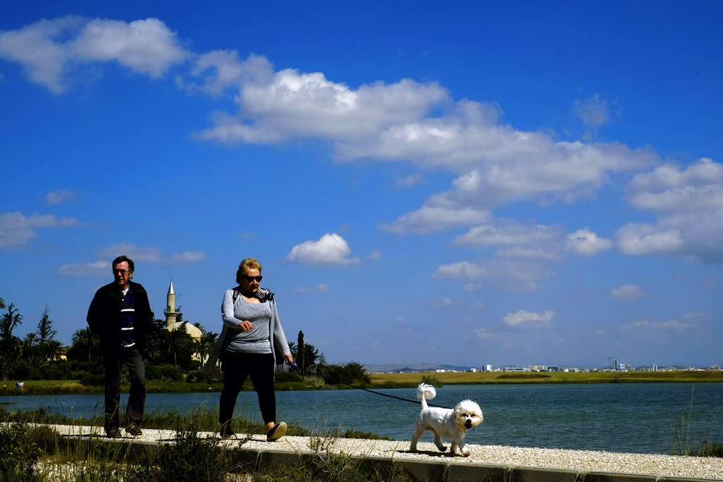 A couple with their dog walk by the salt lake, with the Hala Sultan Tekke Mosque which was built between 1760 and 1796 in the background, in southern coastal city of Larnaca, Cyprus, Thursday, April 18, 2019. (AP Photo/Petros Karadjias)