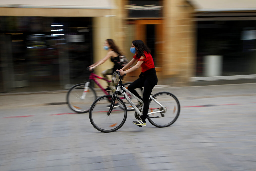 Woman wearing masks ride their bicycles through Ledra Street, a busy shopping thoroughfare in the medieval center of capital Nicosia, Cyprus, on Thursday, May 7, 2020. The rhythms of daily life began returning to normal this week as Cypriot government authorities began rolling back a stay-at-home order to contain the spread of the coronavirus, allowing people to go out three times daily although a night time curfew remains in a effect until May 21. (AP Photo/Petros Karadjias)
