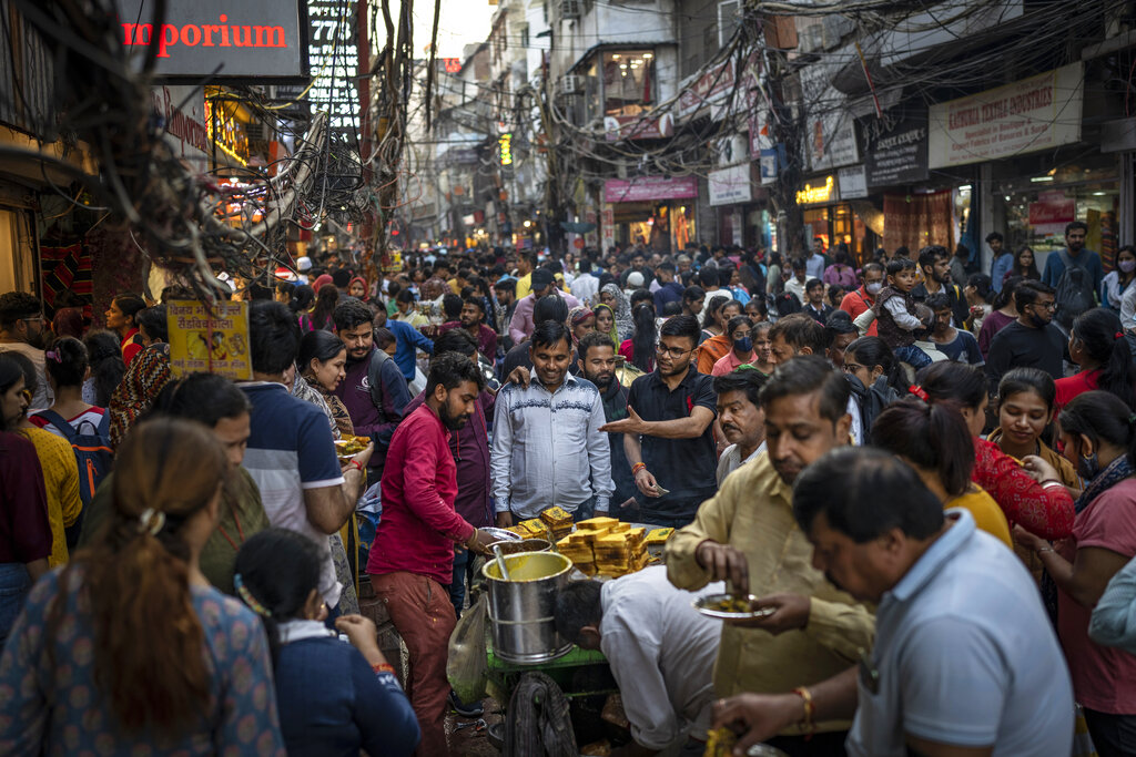 People eat street food as shoppers crowd a market in New Delhi, India, Saturday, Nov. 12, 2022. The world's population is projected to hit an estimated 8 billion people on Tuesday, Nov. 15, according to a United Nations projection. (AP Photo/Altaf Qadri)