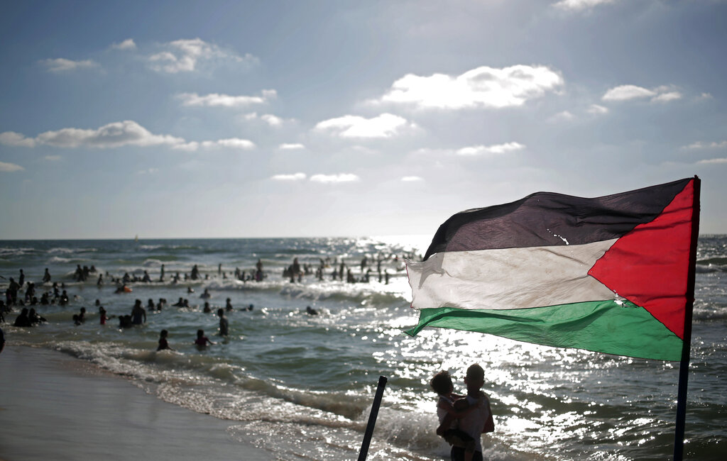 In this Monday, June 23, 2014 photo, a Palestinian flag waves as people enjoy a summer day at the beach of Gaza City.(AP Photo/Khalil Hamra)