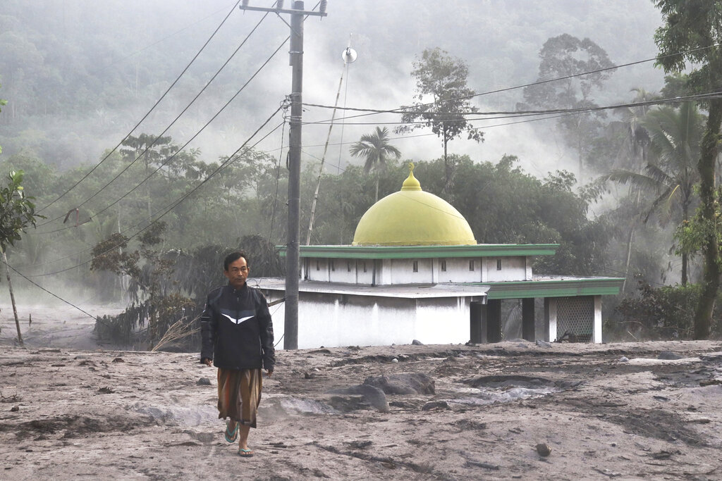 A man walks past a mosque partially covered in volcanic ash from the eruption of Mount Semeru in Kajar Kuning village in Lumajang, East Java, Indonesia, Monday, Dec. 5, 2022. Indonesia's highest volcano on its most densely populated island released searing gas clouds and rivers of lava Sunday in its latest eruption. (AP Photo/Imanuel Yoga)